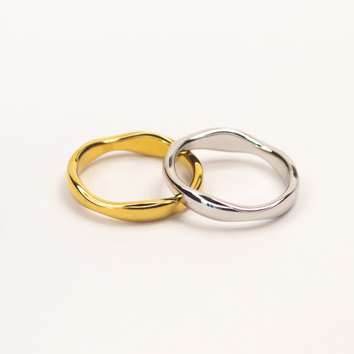 Two wavy, fluid-shaped rings, one in polished yellow gold and the other in polished silver, interlocking on a clean white background.